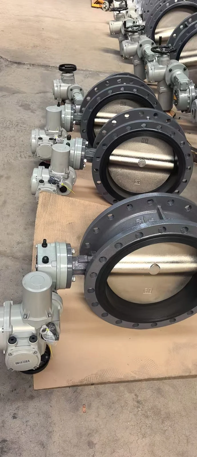 A row of dark-coloured flanged butterfly valves fitted with actuators