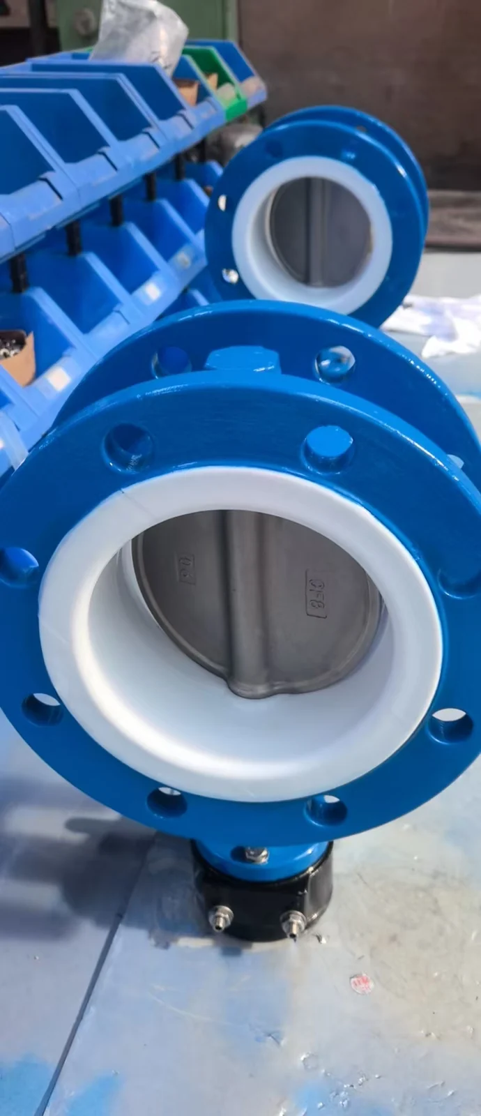 A blue flanged butterfly valve with a white inner lining in a workshop